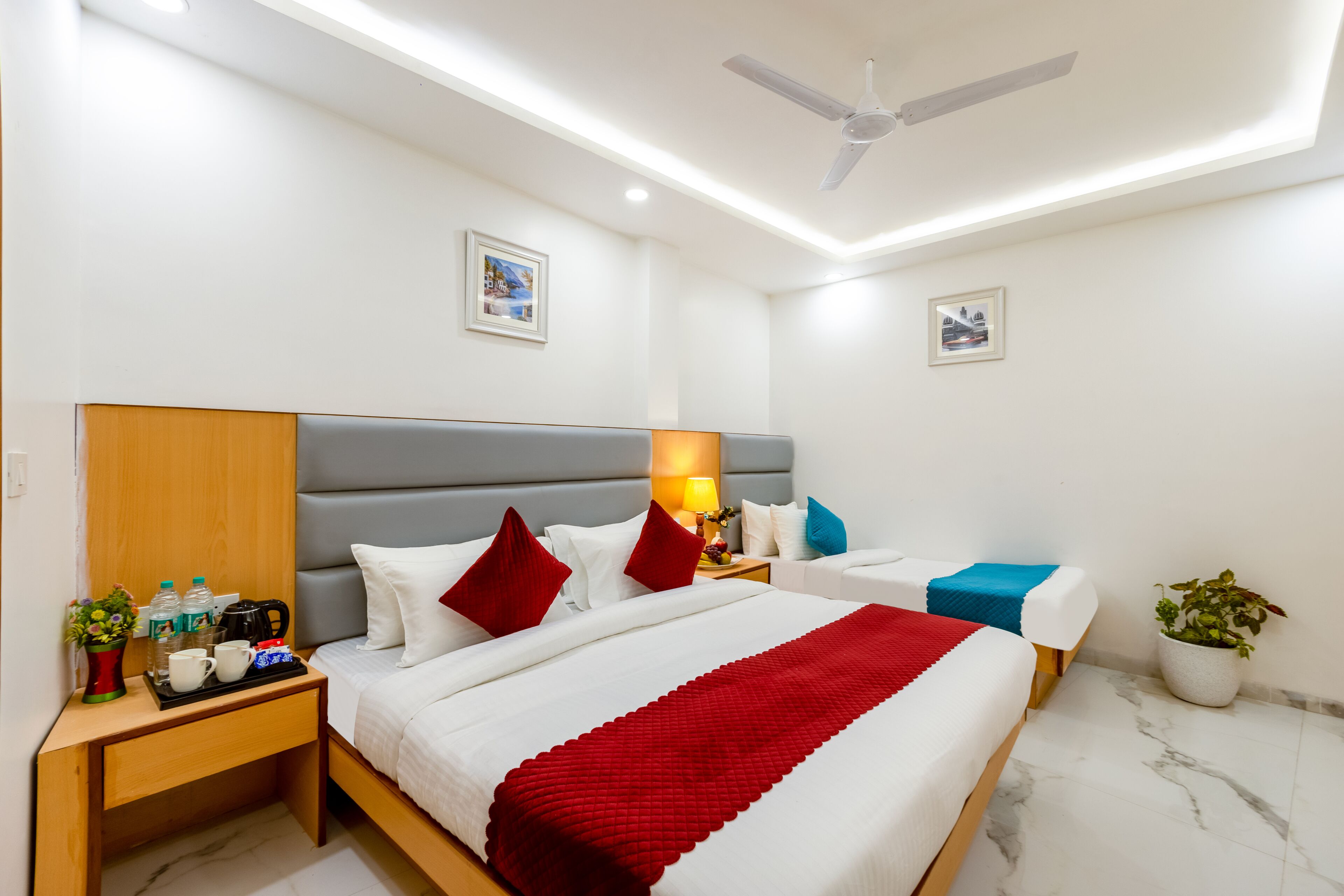 A hotel room with a bed, bedside tables, a ceiling fan, and a potted plant.
