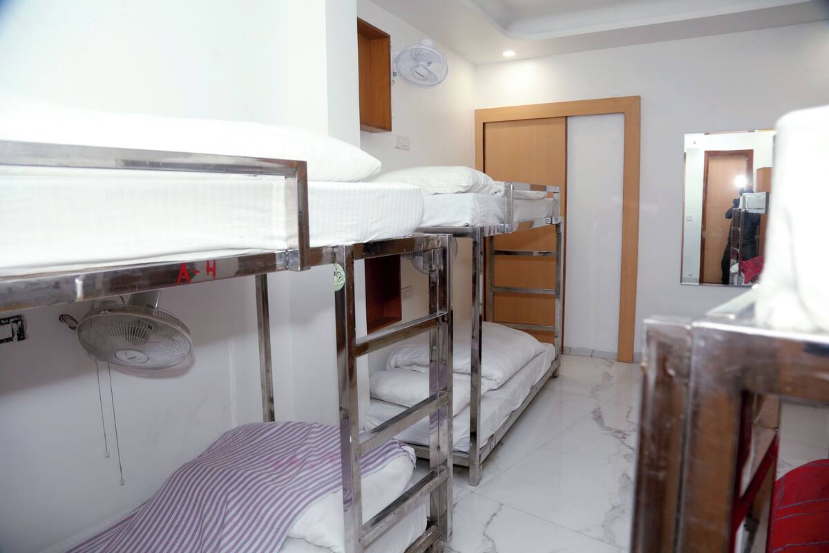 Ein Schlafsaalzimmer mit Etagenbetten, einem Ventilator, einer Holztür und einem Spiegel.