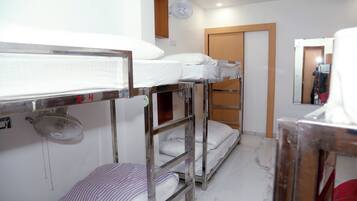 Une chambre de dortoir avec des lits superposés, un ventilateur, une porte en bois et un miroir.