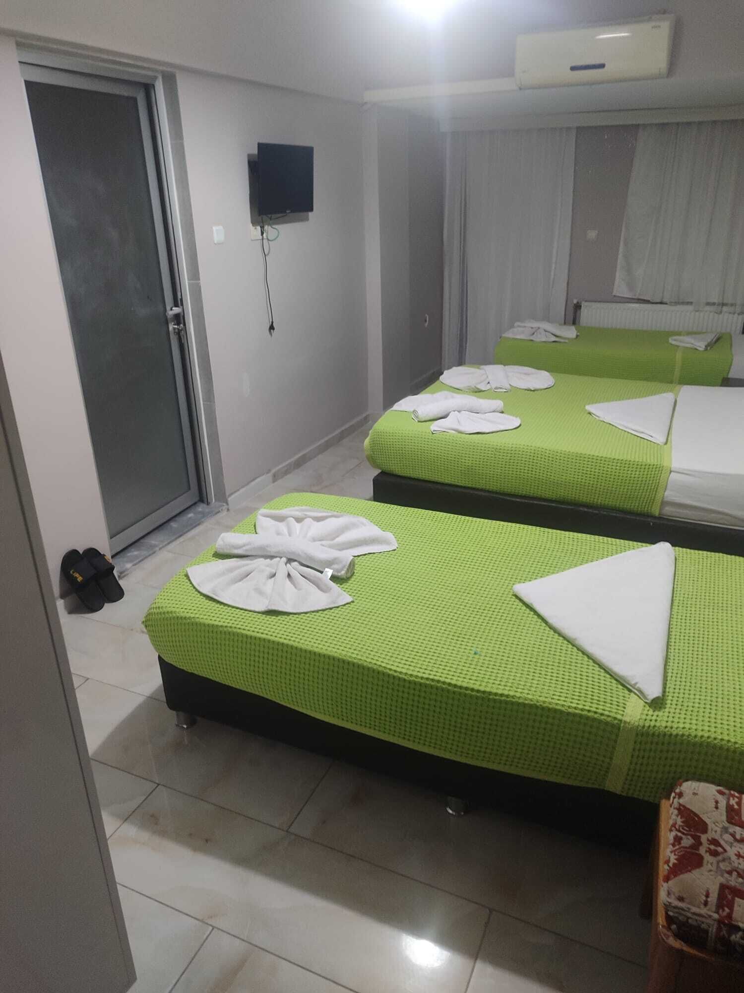 A hotel room with two beds, a TV, a door, and a pair of slippers.