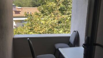 Varanda com mesa e duas cadeiras, vista para árvores e edifícios, e um batente de porta.