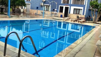 Una piscina al aire libre, sombrillas, sillones reclinables de piscina