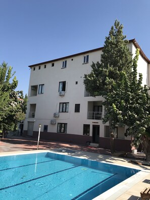 A building with multiple balconies, a swimming pool, and a tree in front. - Anatolia Hotel (Denizli)