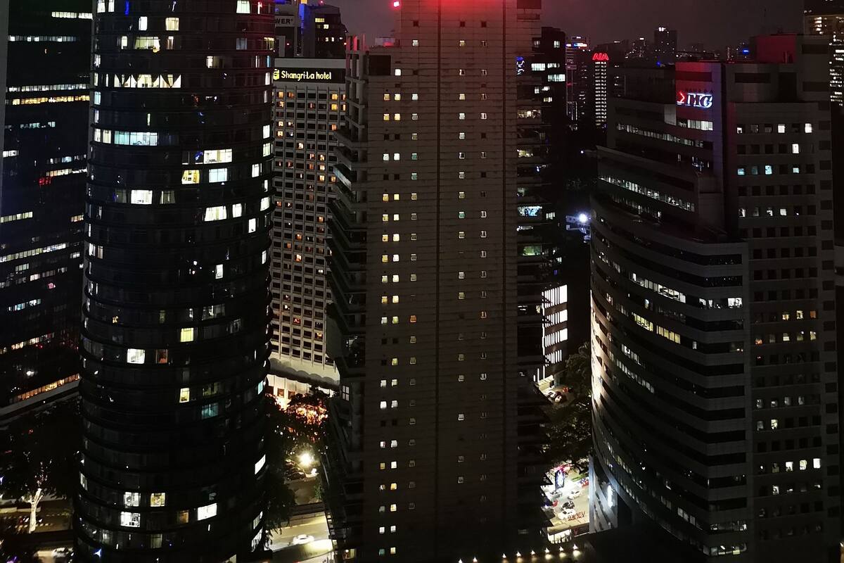 Un immeuble de grande hauteur, doté d’une tour imposante surmontée d’une flèche illuminée en rose et affichant des panneaux indiquant « KL 33 » et le nom d’une clinique dentaire.