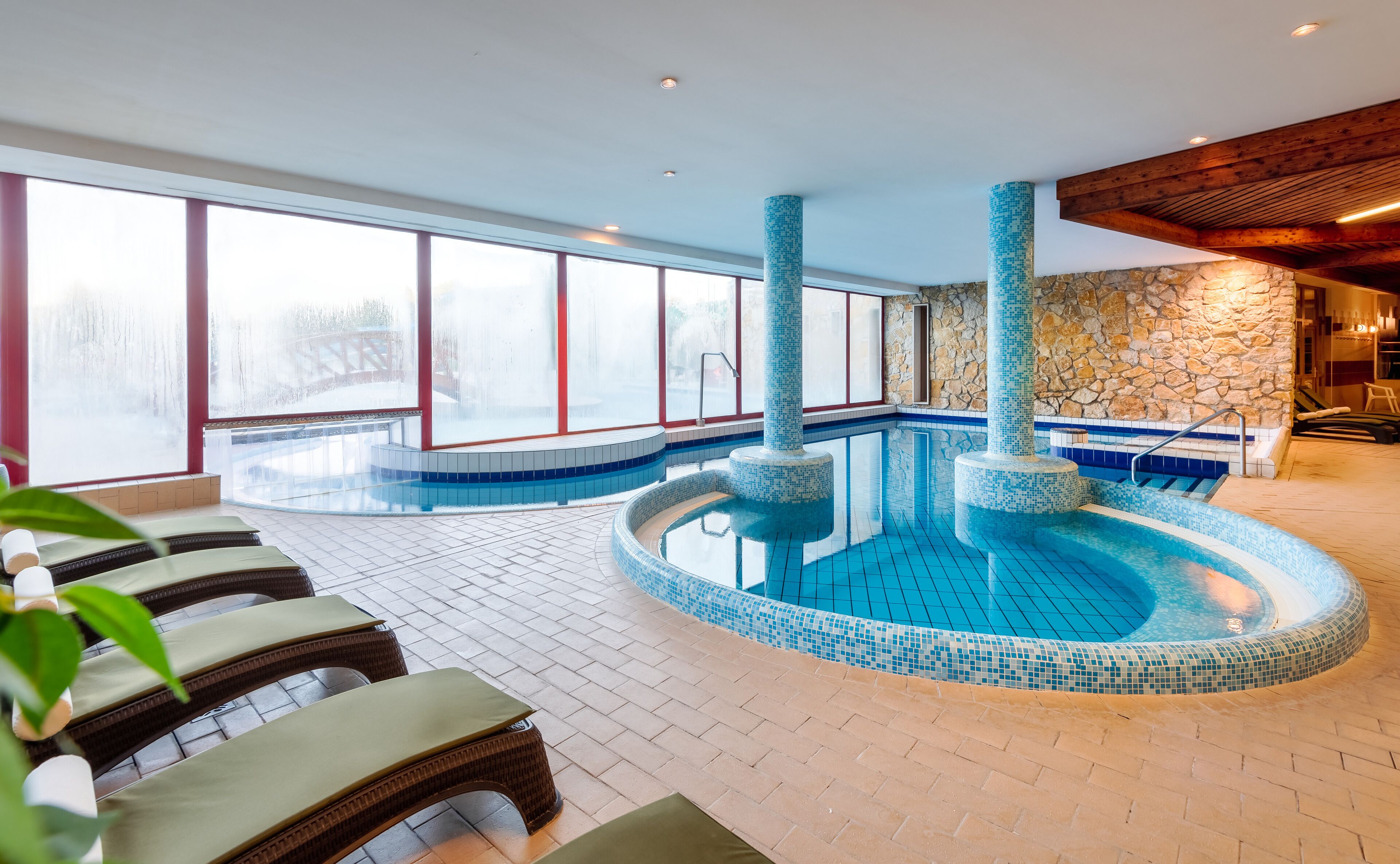 Une piscine intérieure dont les murs sont recouverts de mosaïques et qui présente un mur d’accent en pierre.