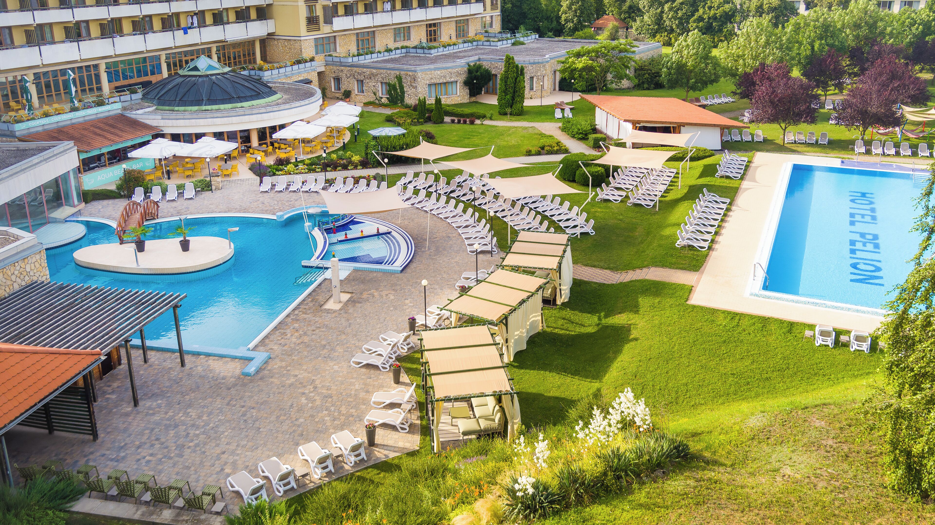 A hotel with a swimming pool, sun loungers, and a garden area.