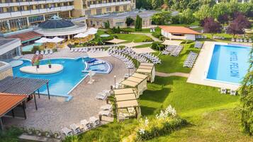 A hotel with a swimming pool, sun loungers, and a garden area.