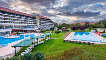 A hotel with multiple swimming pools, a covered seating area, and a well-maintained lawn.