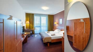 Habitación de hotel con cama, sofá, escritorio, espejo y vistas al exterior.