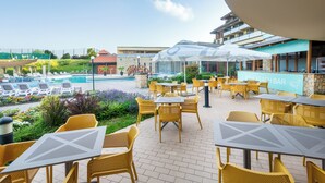 Un área junto a la piscina con sillones de descanso y mesas, un bar y vistas a la piscina.