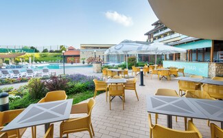 Un área junto a la piscina con sillones de descanso y mesas, un bar y vistas a la piscina.