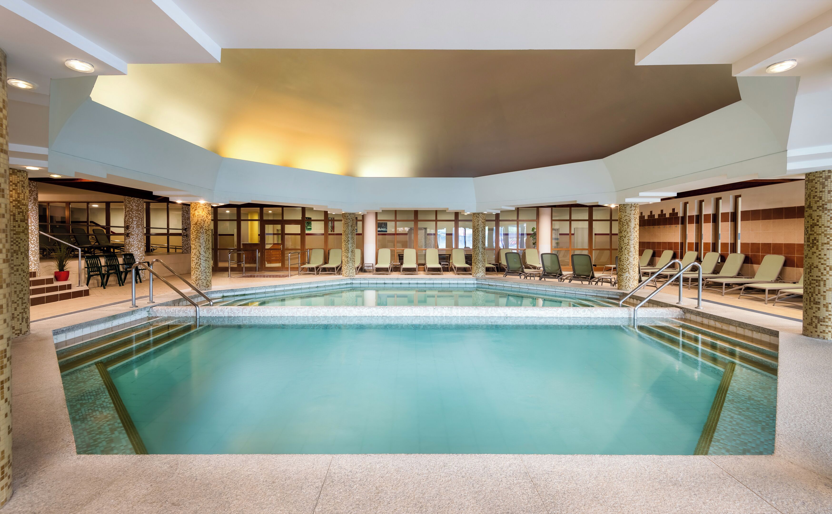 A large indoor swimming pool with lounge chairs and a staircase leading to a lower level.