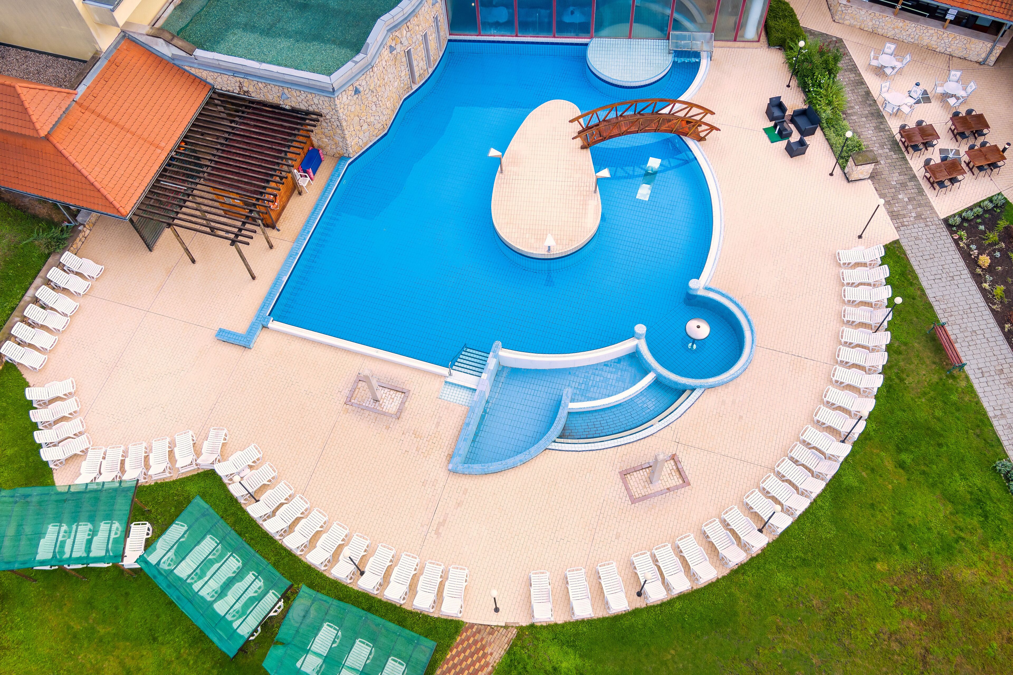 Una piscina con un diseño original en forma de ballena, rodeada de sillas reclinables blancas y una zona de estar cubierta.