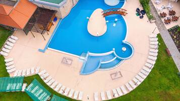 Una piscina con un diseño original en forma de ballena, rodeada de sillas reclinables blancas y una zona de estar cubierta.