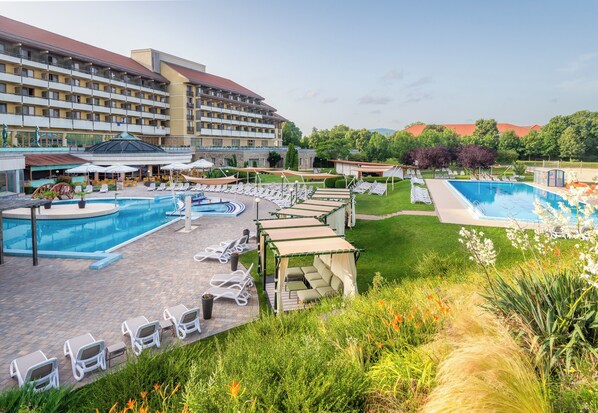 A hotel with a large pool area, multiple lounge chairs, and a well-maintained garden. - Hunguest Hotel Pelion (Tapolca)