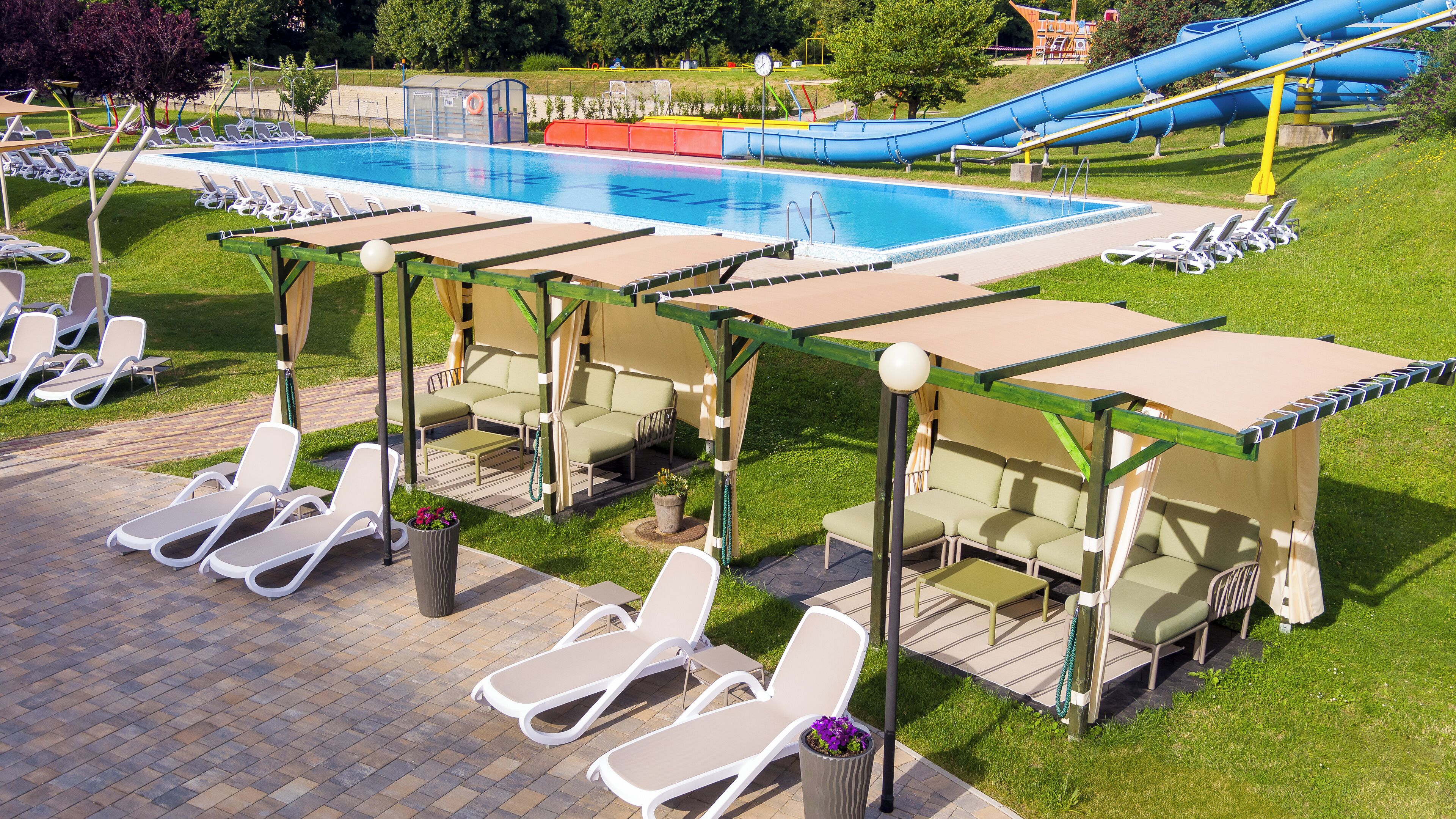 Uma área de piscina com espreguiçadeiras e áreas de descanso à sombra.