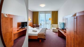 A hotel room with a bed, a TV, a desk with a lamp, and a window with curtains.