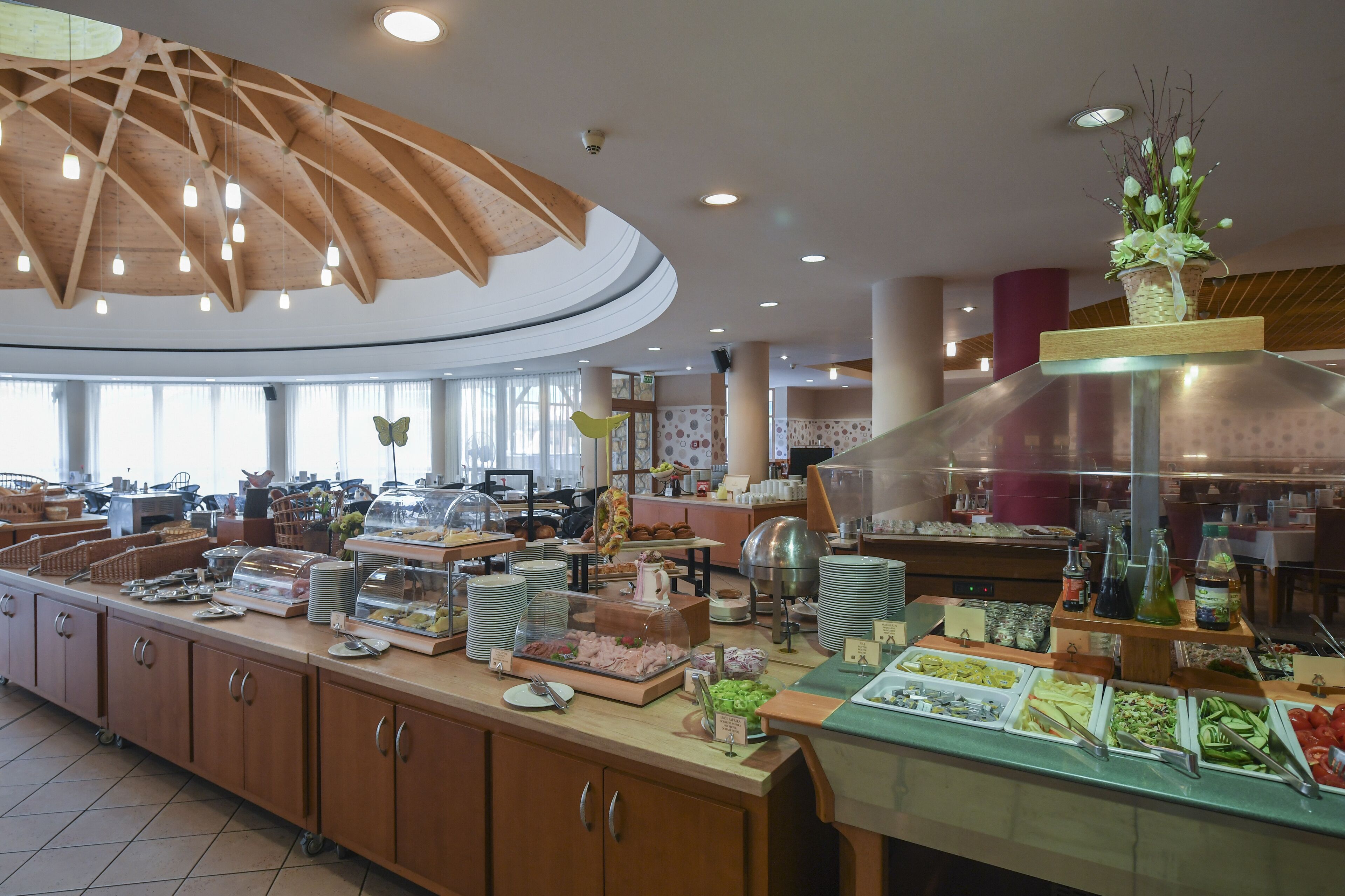 Een buffetgedeelte met diverse food stations, een houten plafond en een groot raam dat natuurlijk licht binnenlaat.