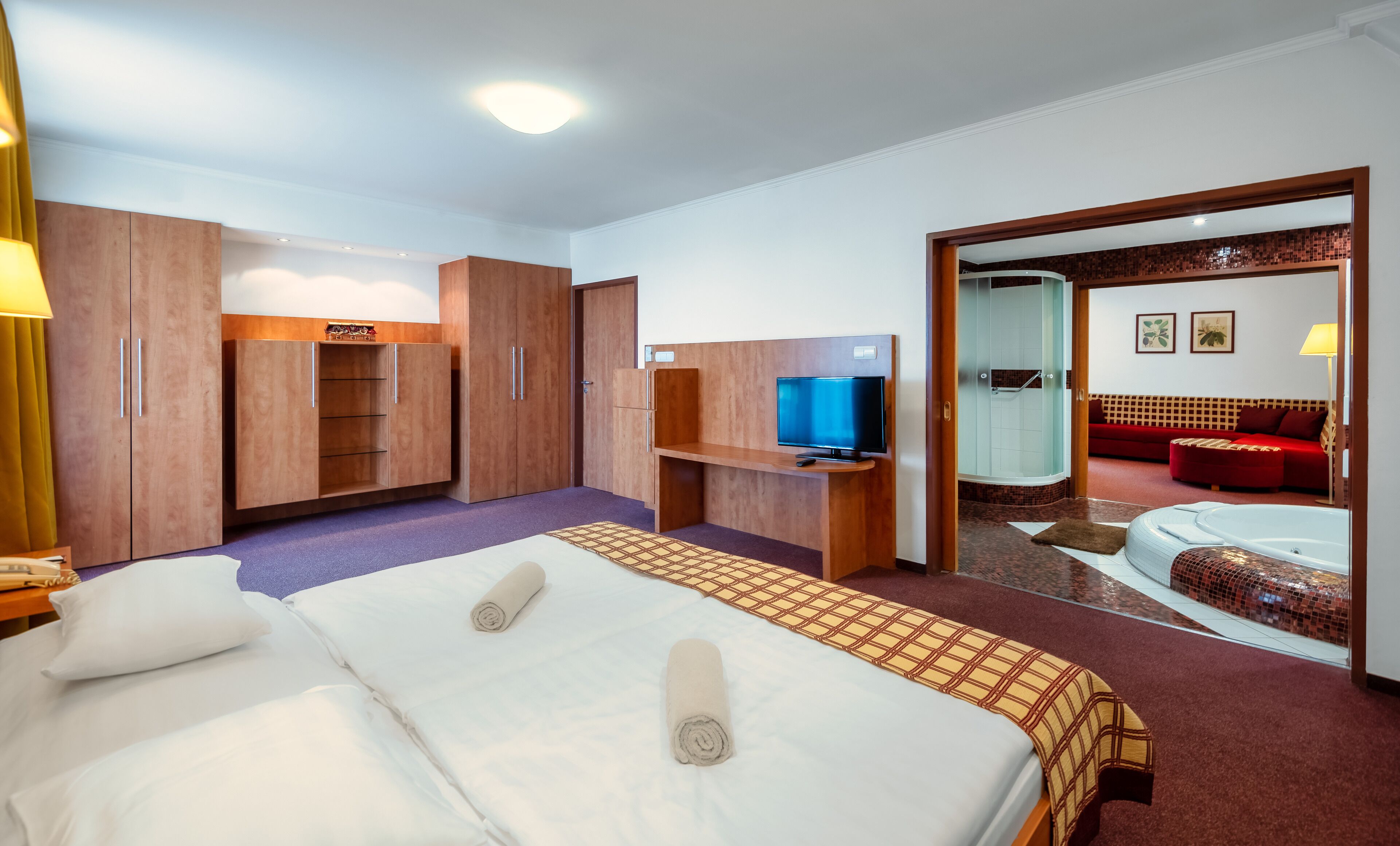 Ett hotellrum med två sängar, en tv, en dusch och en röd soffa.