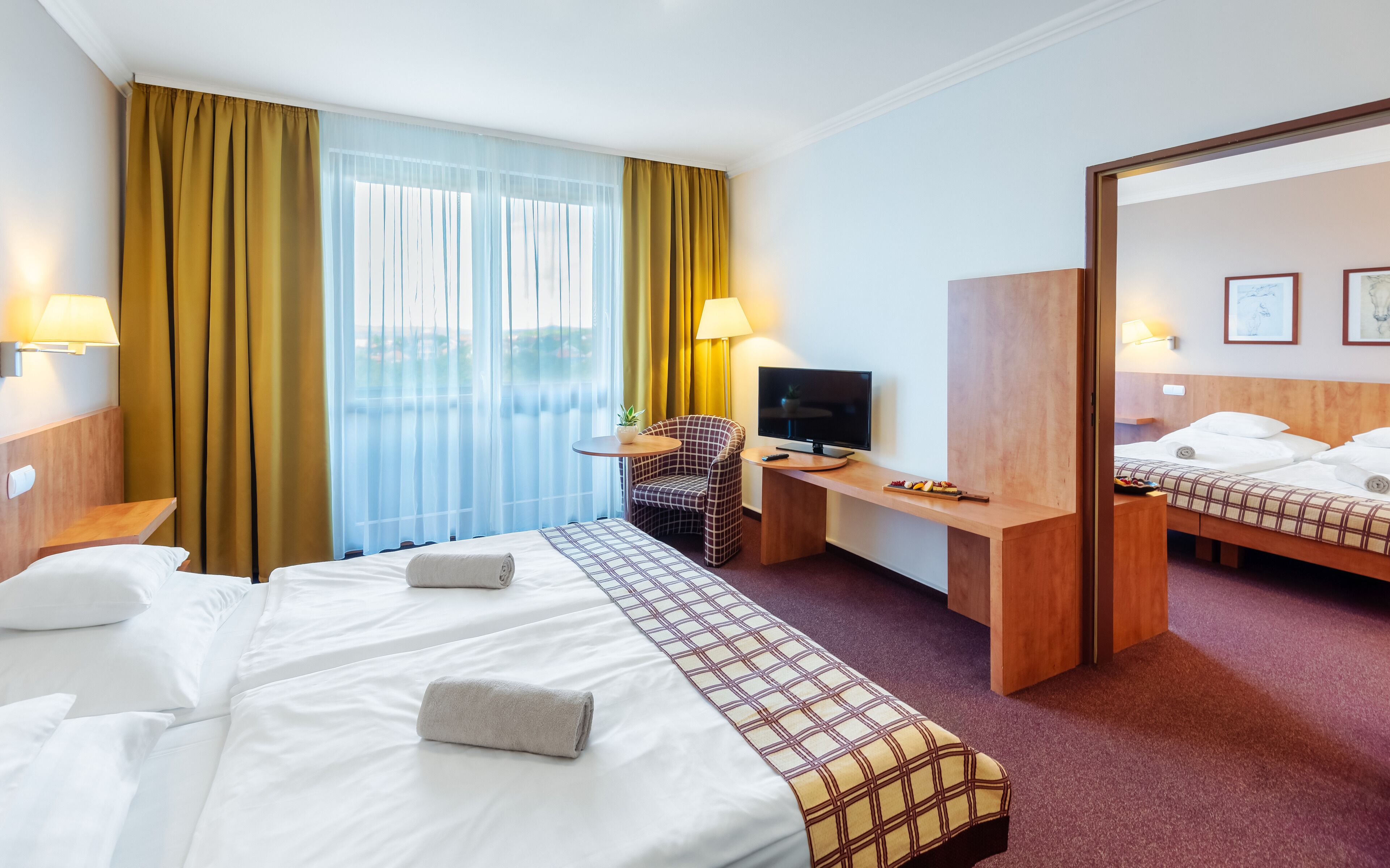 A hotel room with a large bed, a desk with a TV, a chair, and a mirror.