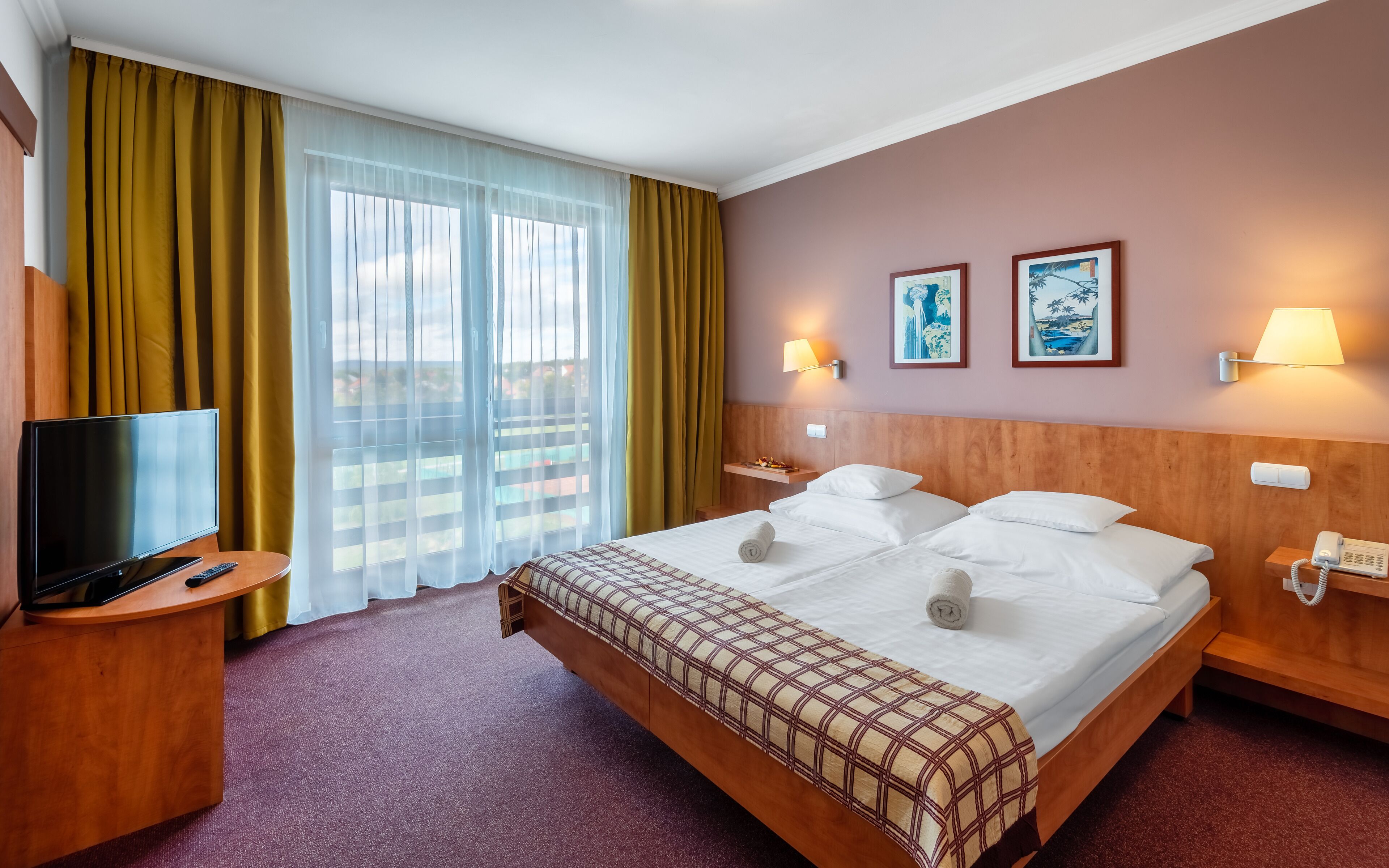Ein Hotelzimmer mit einem großen Bett, einem Fernseher, einem Nachttisch, einer Lampe und einem Telefon.