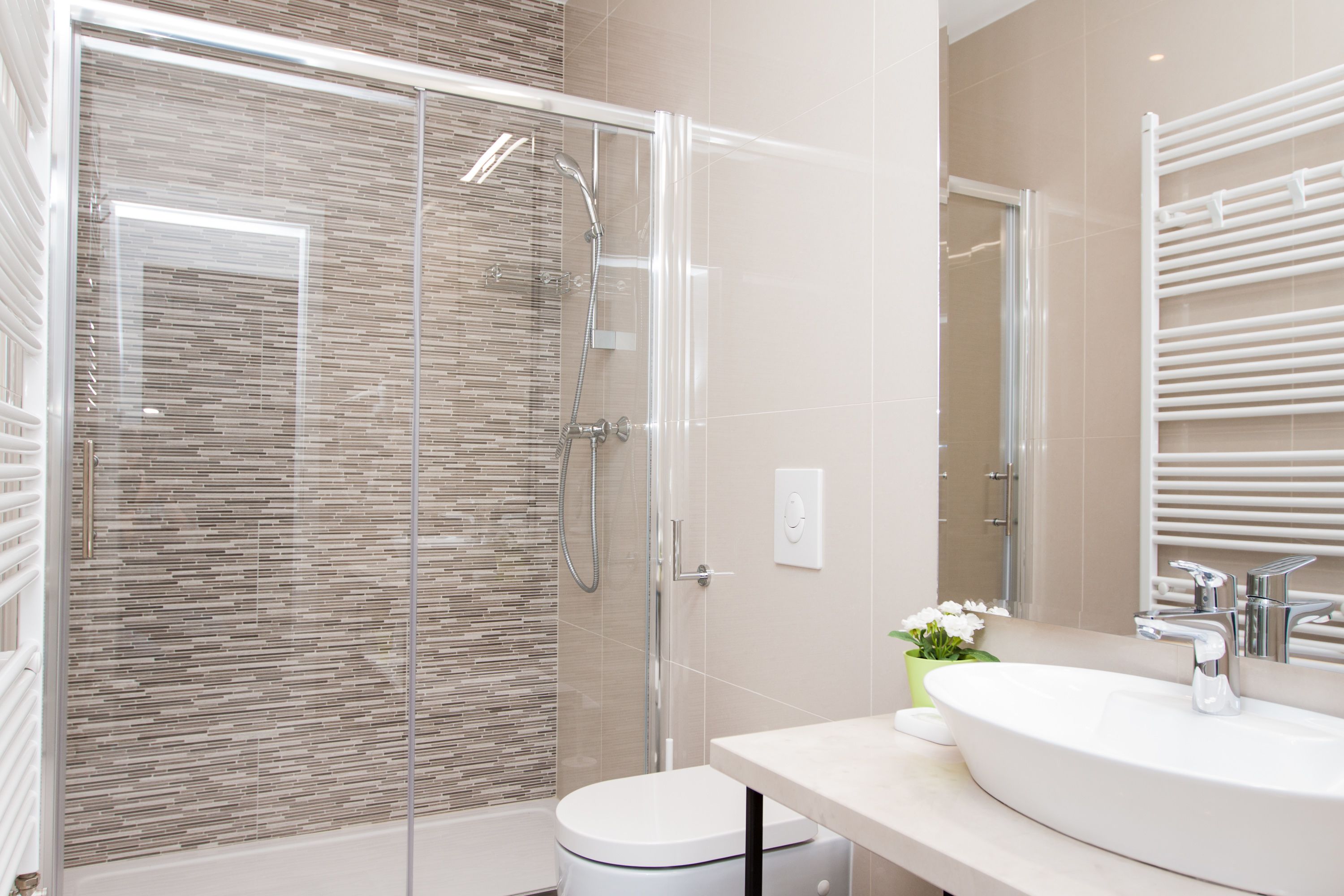 Un baño moderno con ducha envuelta en vidrio, un lavamanos blanco y un espejo con toalleros.