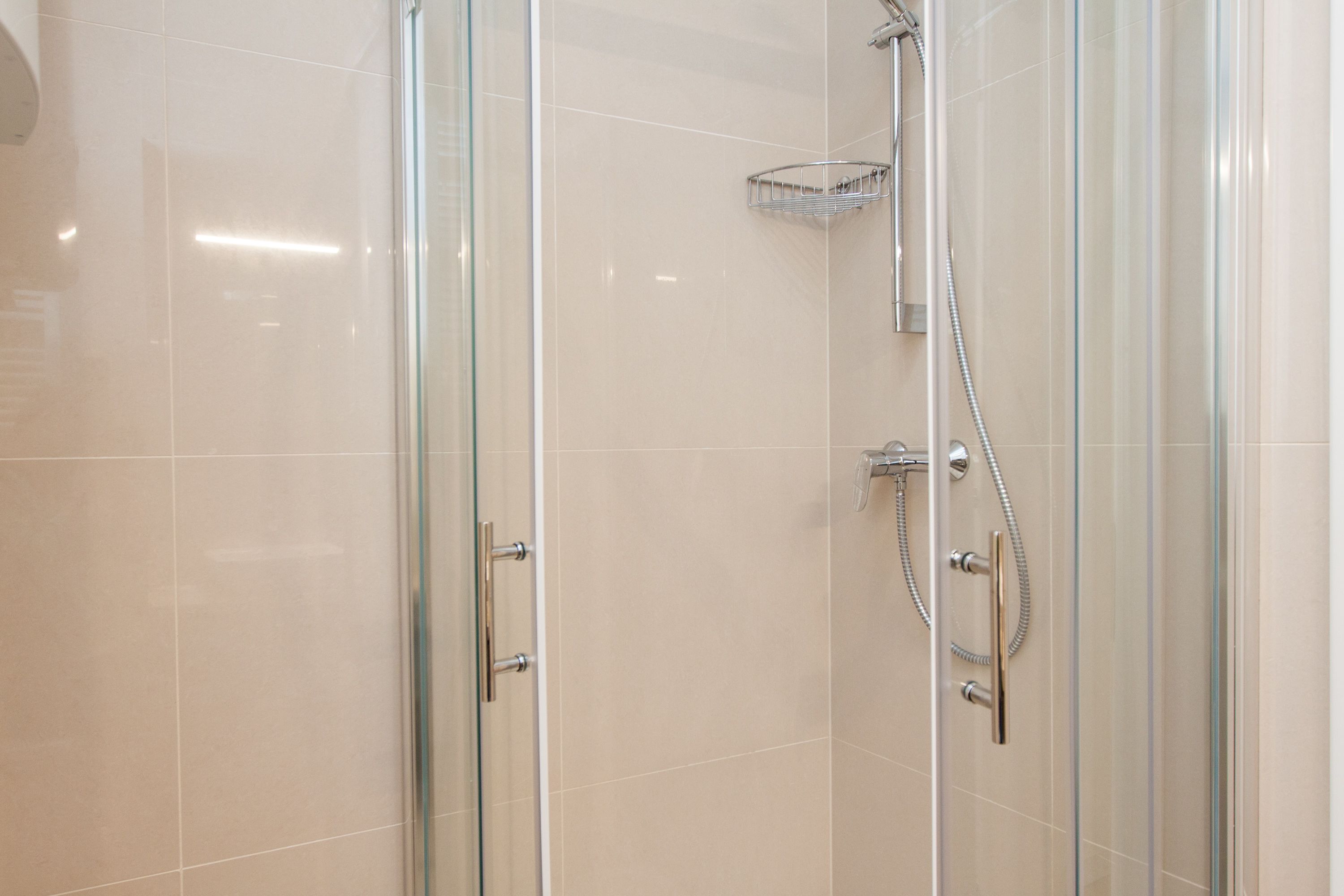 A glass-enclosed shower with a handheld showerhead and a wall-mounted faucet.