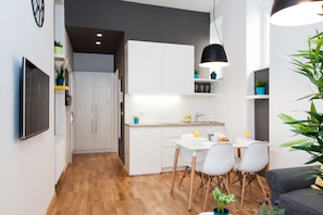 A modern kitchen with white cabinets, a dining area with a table and chairs, and a grey sofa.