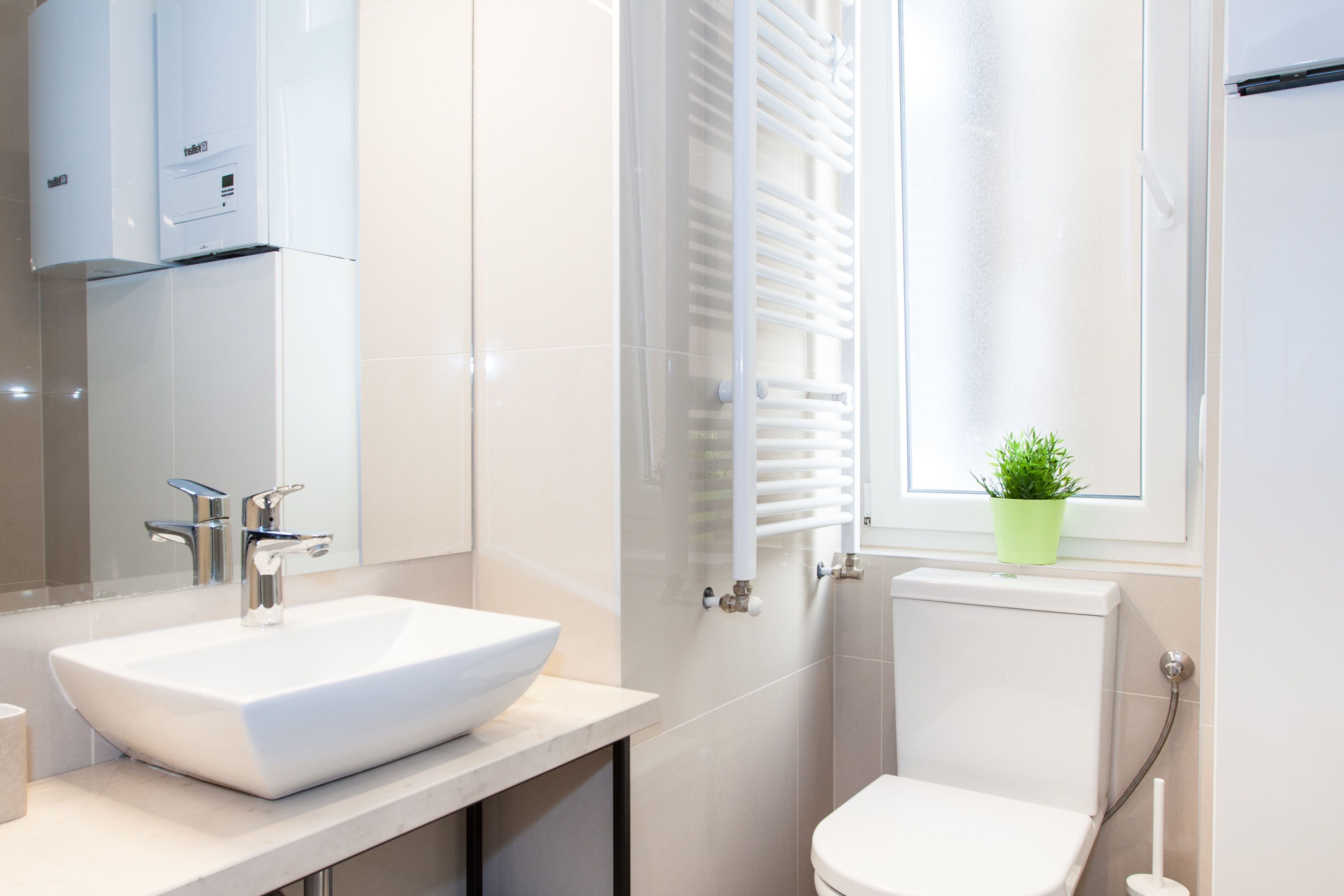 Un bany modern amb un lavabo blanc, un vàter i una finestra amb una planta en test.