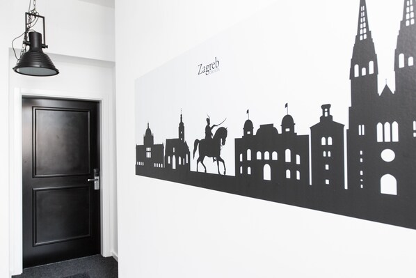 Uma porta preta com um candeeiro acima e o perfil de uma cidade com a palavra "Zagreb" na parede.
