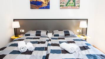 A double bed with a checkered bedspread, two pillows, two bedside lamps, and two rolled towels on the bed.