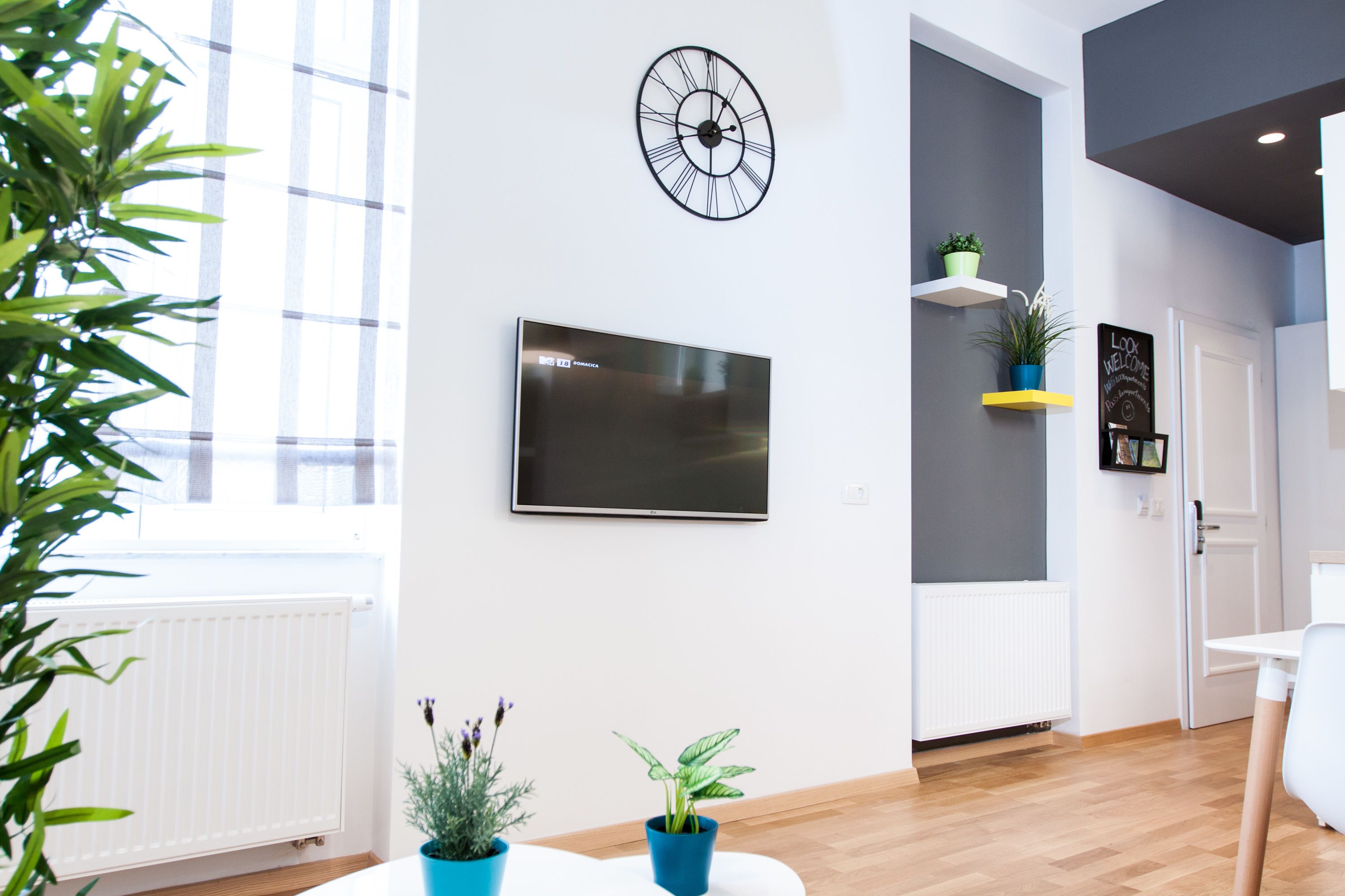 Un interior moderno con un televisor de pantalla plana grande, un reloj de pared y plantas en macetas.