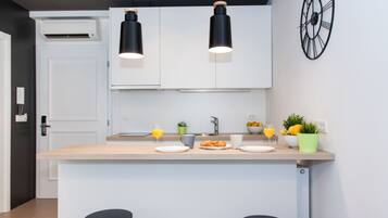 Uma cozinha moderna com armários brancos, uma ilha central com banquetas, uma pia e um relógio na parede.