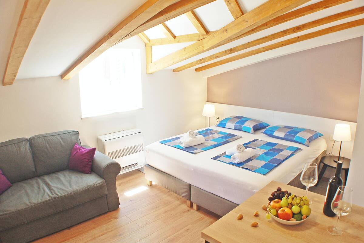 Une chambre à coucher avec un lit, un canapé, une table avec des fruits et des verres, et une fenêtre.