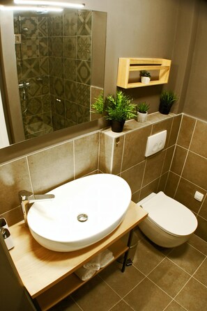 A bathroom with a white sink, a toilet, and a shower area with patterned tiles. There are plants on a shelf above the toilet. - DUMA Apartments Šibenik (Sibenik)