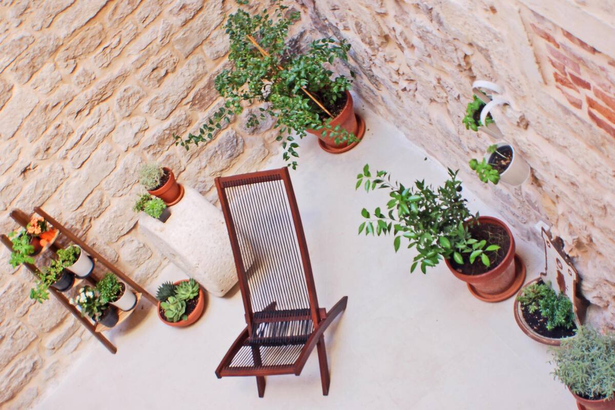 Un mur de pierres avec des plantes en pot et une chaise en bois.