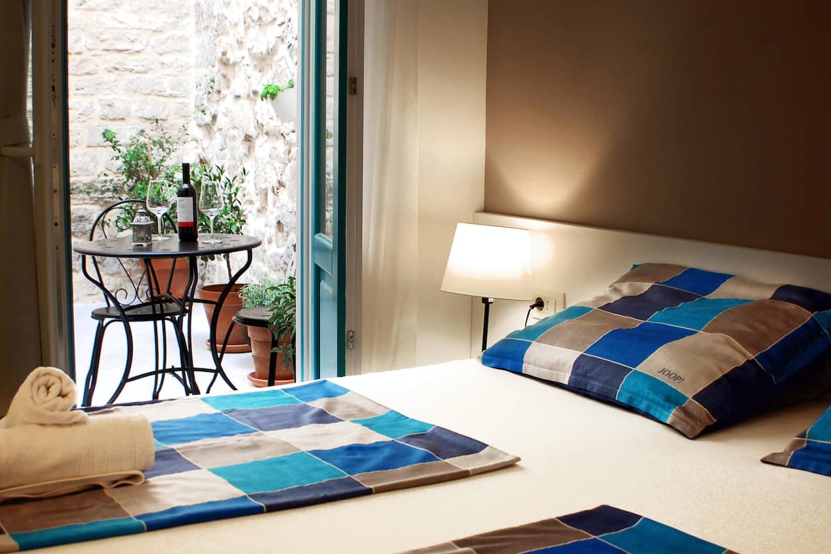 Une chambre d’hôtel avec un lit, une table de chevet avec une lampe, une petite table avec une bouteille et des verres, et une vue sur l’extérieur.