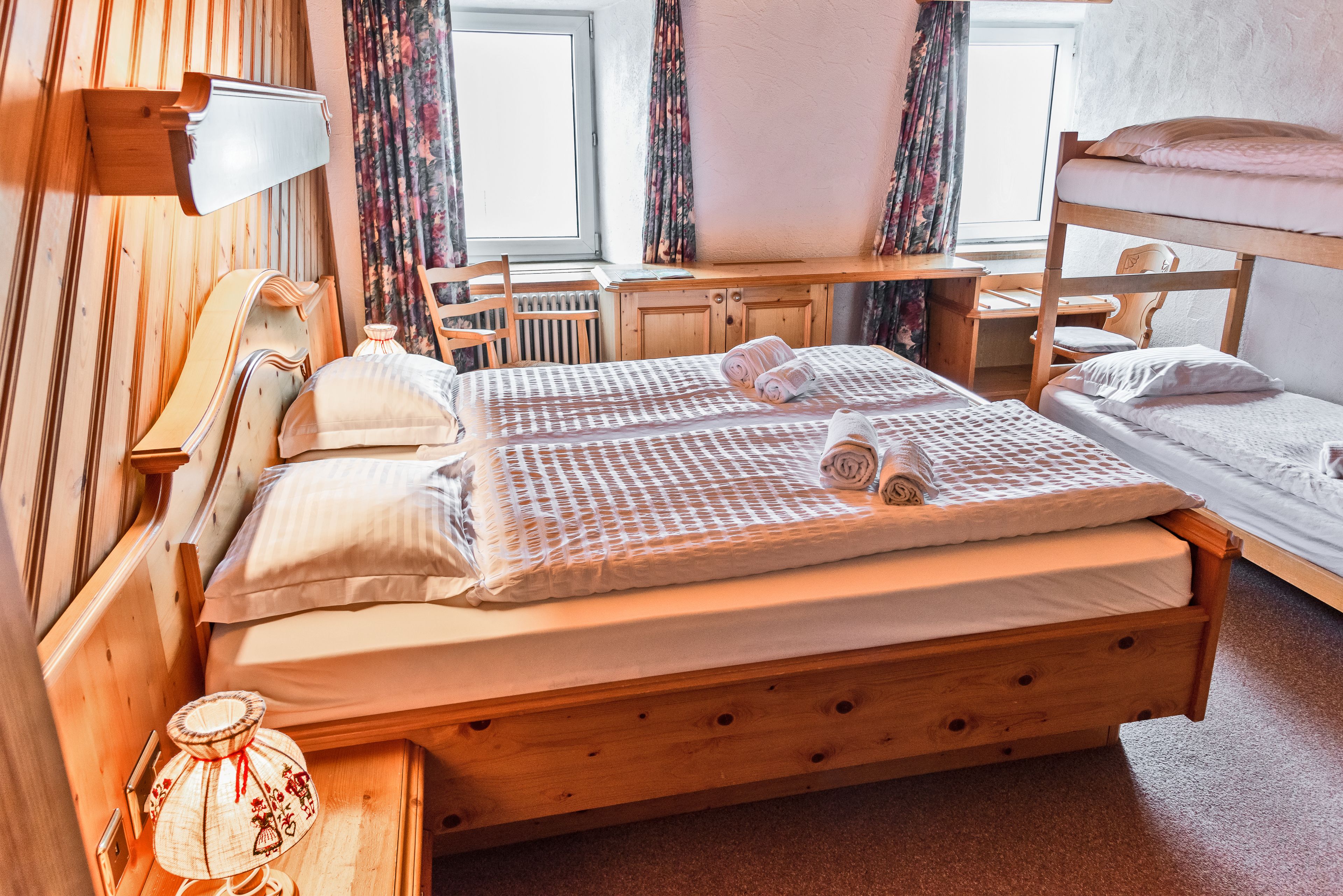 Habitación con literas de madera, escritorio, silla, radiador y ventana con cortinas.