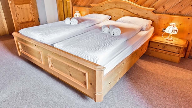 Un grand lit en bois, recouvert de draps blancs, avec deux tables de chevet dotées de lampes.