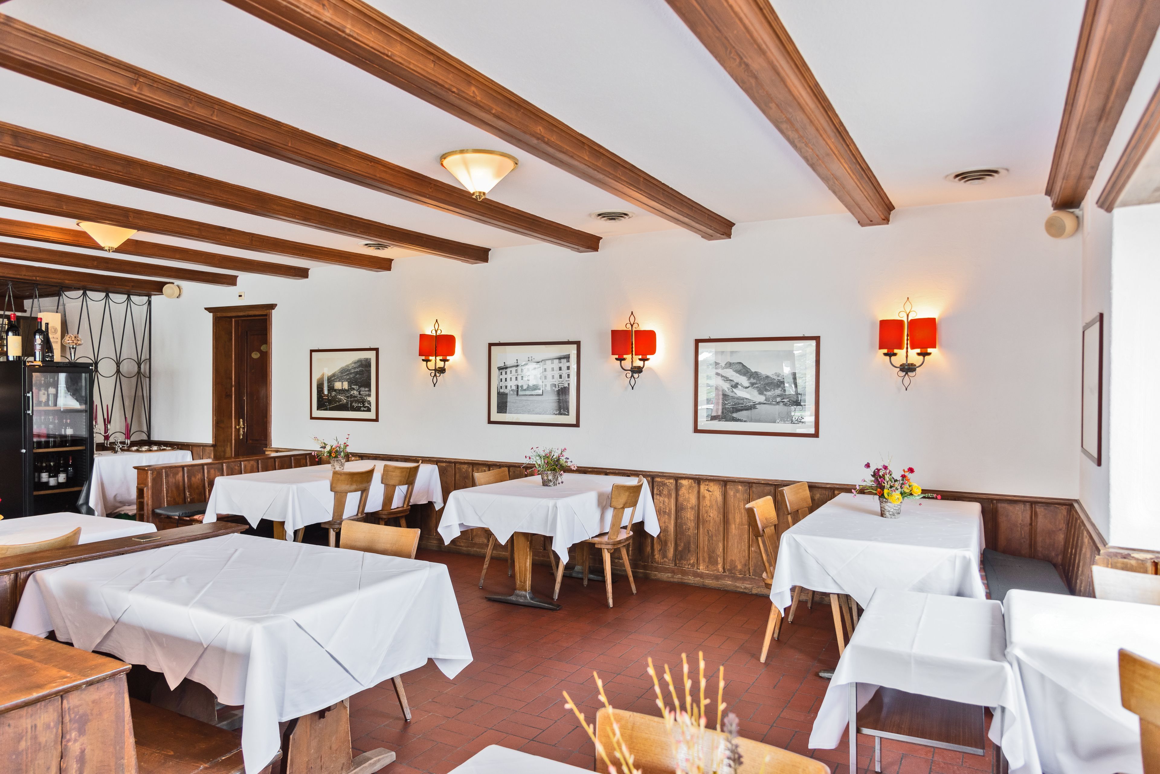 Un restaurante con vigas de madera, mesas blancas y apliques rojos en las paredes.