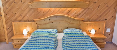 Un lit double avec une tête de lit et des tables de chevet assorties, un plafond en bois et un design simple et épuré.