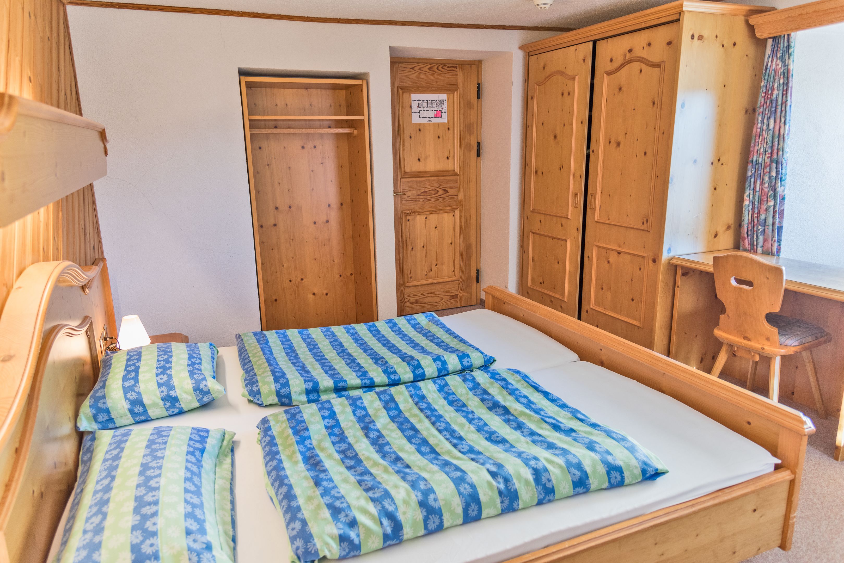 A wooden bed with blue and green striped bedding, wooden wardrobe, and a wooden chair.