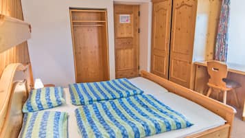 A wooden bed with blue and green striped bedding, wooden wardrobe, and a wooden chair.