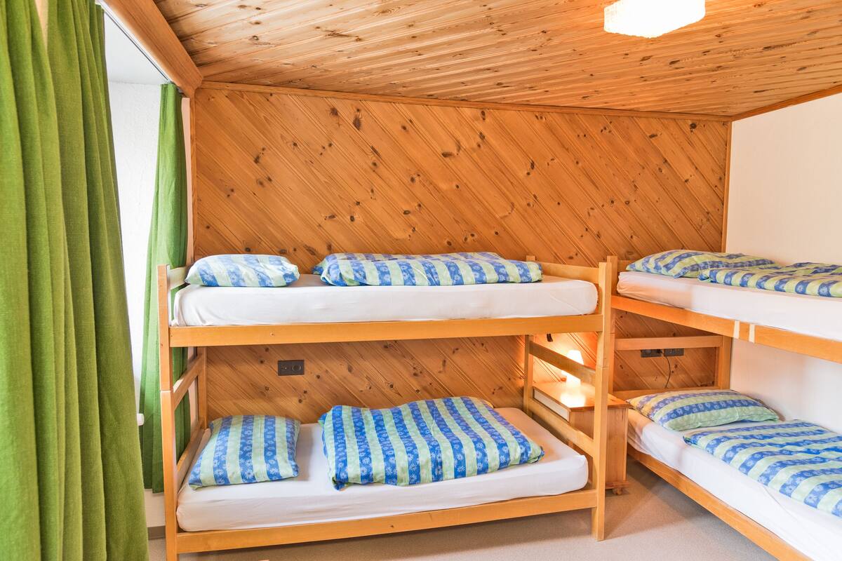 Dormitorio con literas, paredes de madera y cortinas verdes.