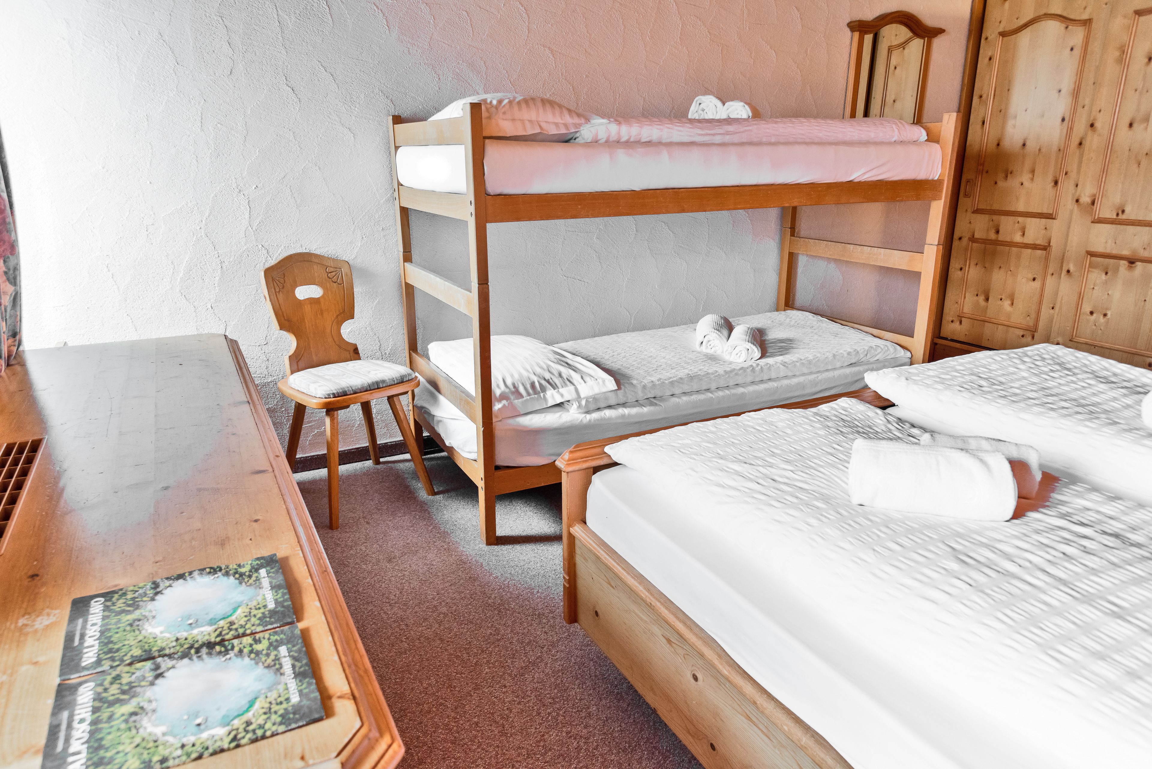 A bunk bed room with a wooden desk and chair, a small table with brochures, and a wardrobe.