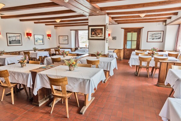 Un restaurante con varias mesas y sillas, vigas de madera en el techo y obras de arte en las paredes.