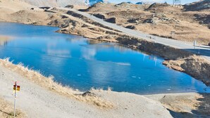 Un ciel bleu dégagé, avec des lignes électriques, une route et une étendue d’eau dans une région montagneuse.