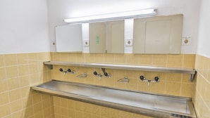 Une salle de bain avec des murs recouverts de carreaux jaunes, un évier en acier inoxydable et un miroir au-dessus.
