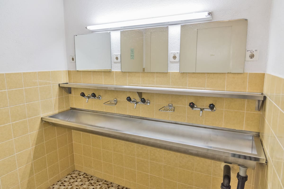 Un baño con paredes de azulejos amarillos, un lavamanos de acero inoxidable y un espejo encima.