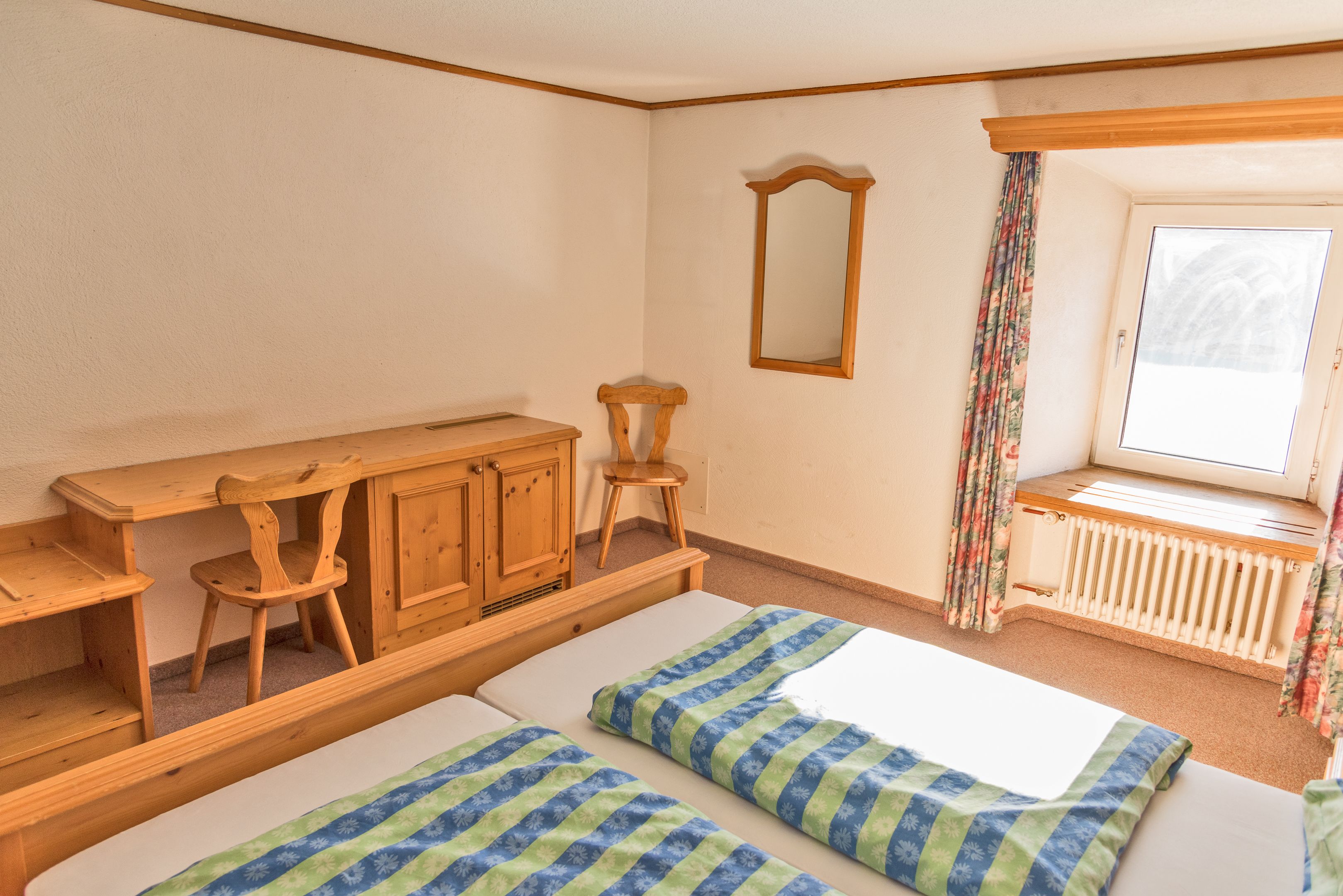 Een kamer met twee bedden, houten meubels, een raam met gordijnen en een radiator.